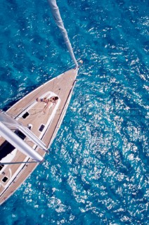 View from masthead of woman lying on deck of anchored cruising yacht