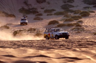 Two trucks drive in convoy through the desert, Dubai - United Arab Emirates.