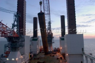 Construction of Windfarm on the Kentish flats in the Thames estuary off Whitstble Kent. Onboard the construction ship Resolution during the foundation process, where the Monopile is hammered in to the seabed with a hydraulic hammer and the transition piece lowered onto the monopile, picture shows monopile being craned into place ready for piling into seabed .