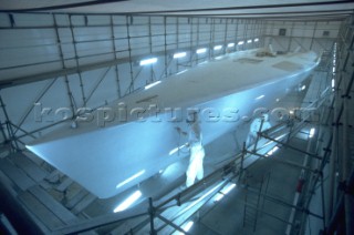Boatyard workers painting the topsides of a superyacht with a spray gun