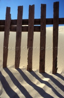 Shadows of fence posts on dry sand