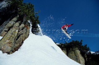 Snowboarder jumping off rocky outcrop.