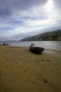 Dinghy on sand at Salcombe Estuary with mist on hills in distance, UK