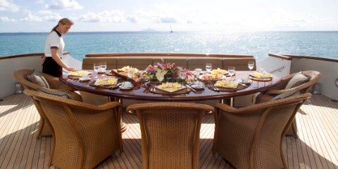 Stewardess sets dining table on aft deck of superyacht