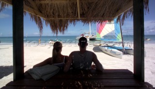 Two people under the shade of a beach hut, Caribbean