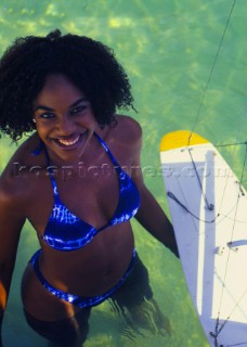 Woman in blue bikini standing in shallow water holding model yacht