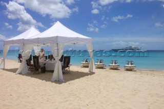 Jet skis lined up on sandy beach next to table set for lunch under white awning