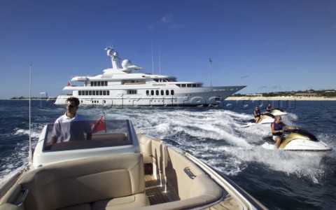 Jet skiers and tender driving away from anchored superyacht