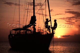 Couple sitting on bow of anchored yacht at sunset