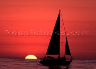 A yacht furling its sails at sunrise