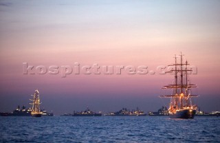 Square riggers at anchor with Trafalgar 200 warship fleet in background at sunset