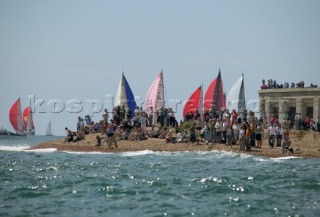 The Fasntet fleet pass through the Solent by Hurst Castle watched by a crowd on the beach.