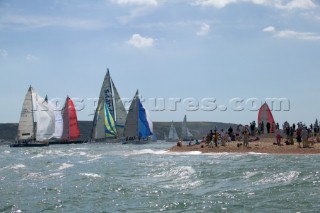 The Fasntet fleet pass through the Solent by Hurst Castle watched by a crowd on the beach.