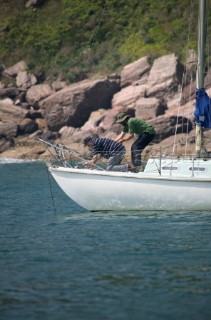 Two men pull up an anchor on a small cruising yacht