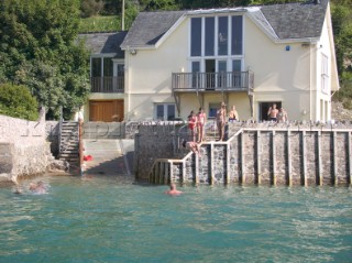 Children and kids jump and dive into the water from a wall in front of a luxury house in Salcombe Harbour