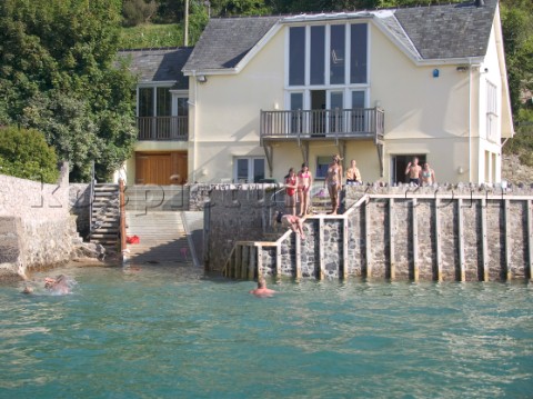 Children and kids jump and dive into the water from a wall in front of a luxury house in Salcombe Ha