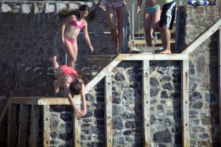 Children and kids jump and dive into the water from a wall in front of a luxury house in Salcombe Harbour