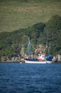 Fishing trawler at anchor in a protected bay in front of green fields