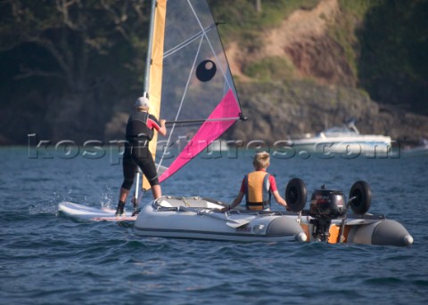 Young boy driving a Zodiac teaching his mother to windsurf