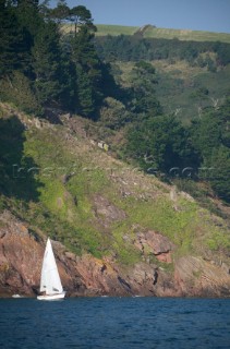 Cruising yacht sailing in front of spectacular rocks and trees in Devon UK