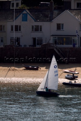 Dinghy sails in front of a house on the waterfront of Salcombe Harbour UK