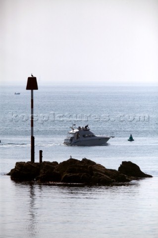 Motor boat passes rocks and red port and green starboard navigation marks leaving Salcombe Harbour