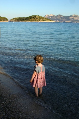 Little girl in pink dress paddling on sandy beach in bay of Formentor Mallorca