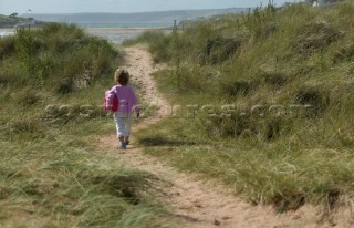 Little girl walking up sandy path at Bantham beach, Devon
