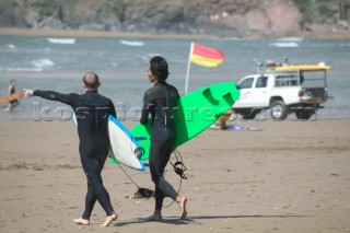 Two surfers head to the water on the beach at Bantham, Devon