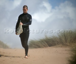 Surfer heads towards sea over sand dunes at Bantham, Devon