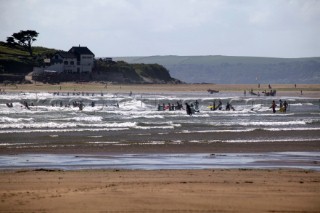 Surfers in waves at low tide. Bantham, Devon