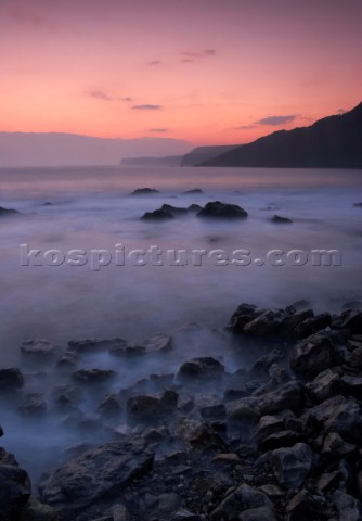 Motion effect of water lapping on shore under pink sky