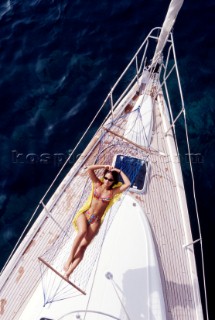 Woman lying in a hammock on the foredeck of a cruising yacht.