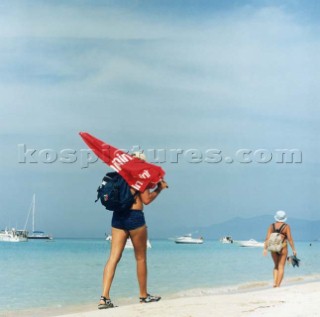 Man walking along sandy beach with red umbrella