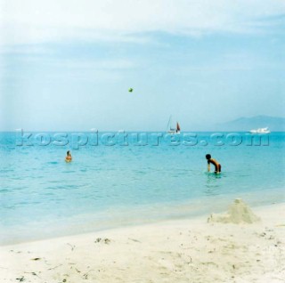 People playing in clear blue sea off sandy beach under clear blue sky
