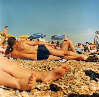 People sunbathing on pebble beach under clear blue skies, Brighton
