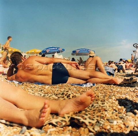 People sunbathing on pebble beach under clear blue skies Brighton