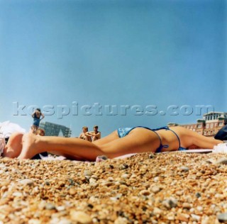 Girl in bikin lying on pebble beach under clear blue sky, Brighton