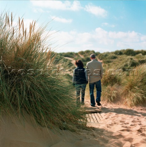 Couple walking through sand dunes on beach at Aberdeen