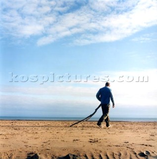 Man dragging driftwood along the beach at Swansea, Wales