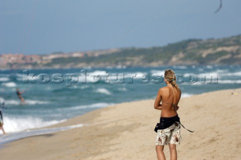 Surfer chick standing on sandy beach looking out to sea
