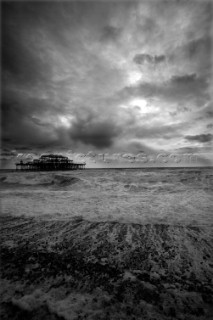 Black and White picture of Brighton Pier taken from beach on a dark cloudy day