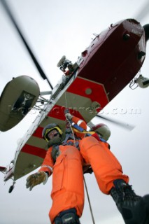 Coastguard rescue worker being lowered from helicopter by winch from below