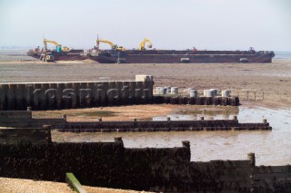 two barges with beach infill unloading there cargo at the low water line, Sea defence building in whitstable kent raising the level of the beach some meters to counter rising sea level and erosion