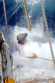 Antigua Classic Yacht Regatta April 2006. Part of sequence of crew member on Aschanti IV working on leeward side as wave comes crashing over side of boat to submerge  him as he holds on to a line