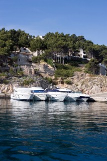 Five powerboats moored at a jetty in front of residential building on a rocky slope