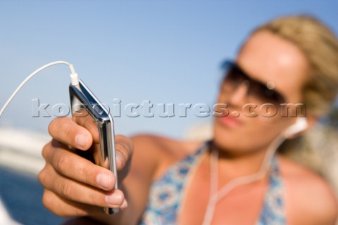 Girl in bikini and sunglasses on boat listens to music playing on an iPod