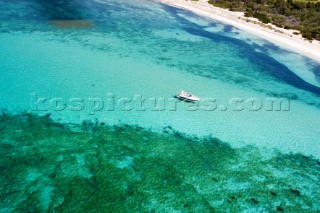 Aerial shot of power boat floating in shallow water near sandy beach