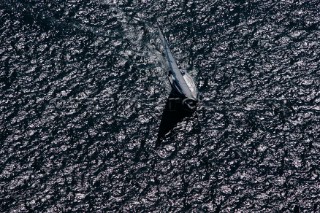 Aerial shot of yacht sailing across a black textured sea