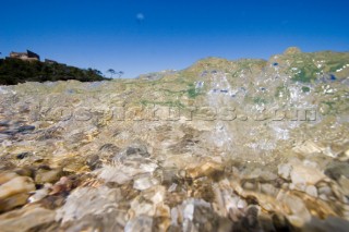 A shallow clear stream tumbles over a bed of pebbles under a sunny blue sky